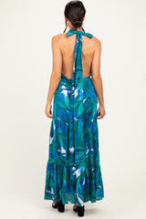 woman wearing a backless maxi dress with a green and blue tropical print and a halter tie at the neck