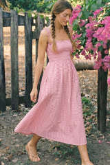 woman wearing a pink and white gingham midi dress with spaghetti straps, walking outdoors near purple flowers