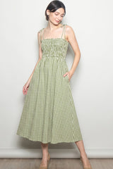 woman wearing a green and white gingham midi dress with adjustable straps and pockets