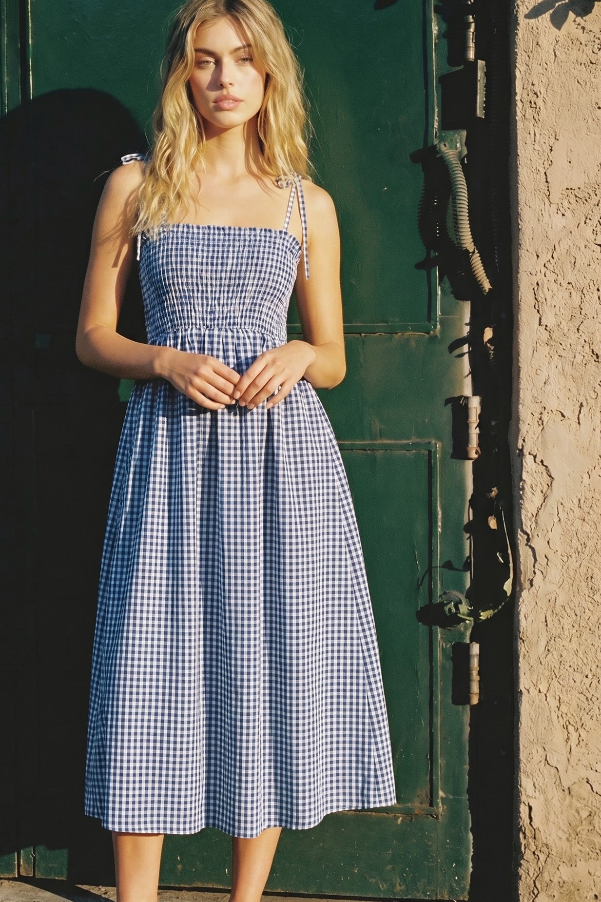 woman wearing a blue and white gingham midi dress with adjustable straps and a smocked bodice