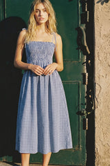 woman wearing a blue and white gingham midi dress with adjustable straps and a smocked bodice