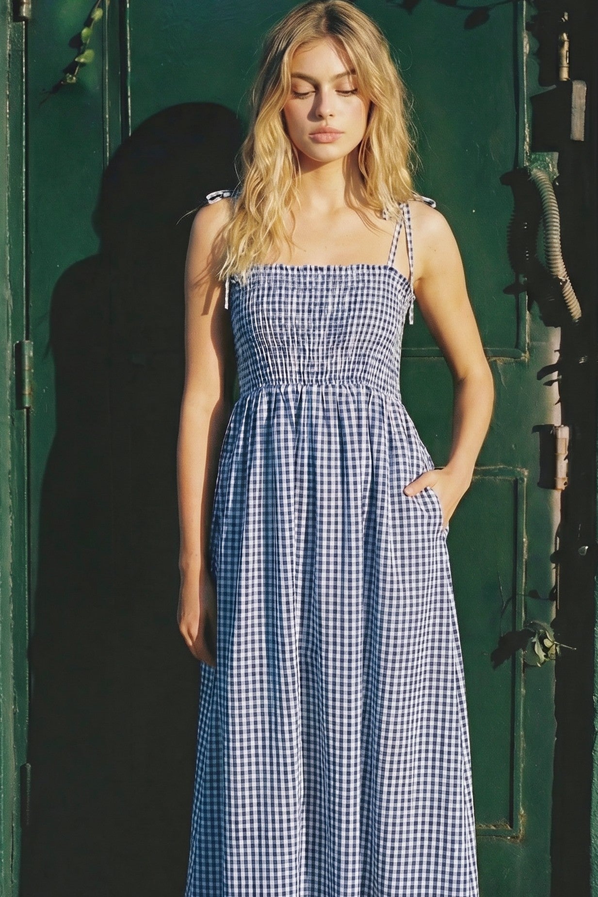 woman wearing a blue and white gingham maxi dress with adjustable straps and side pockets