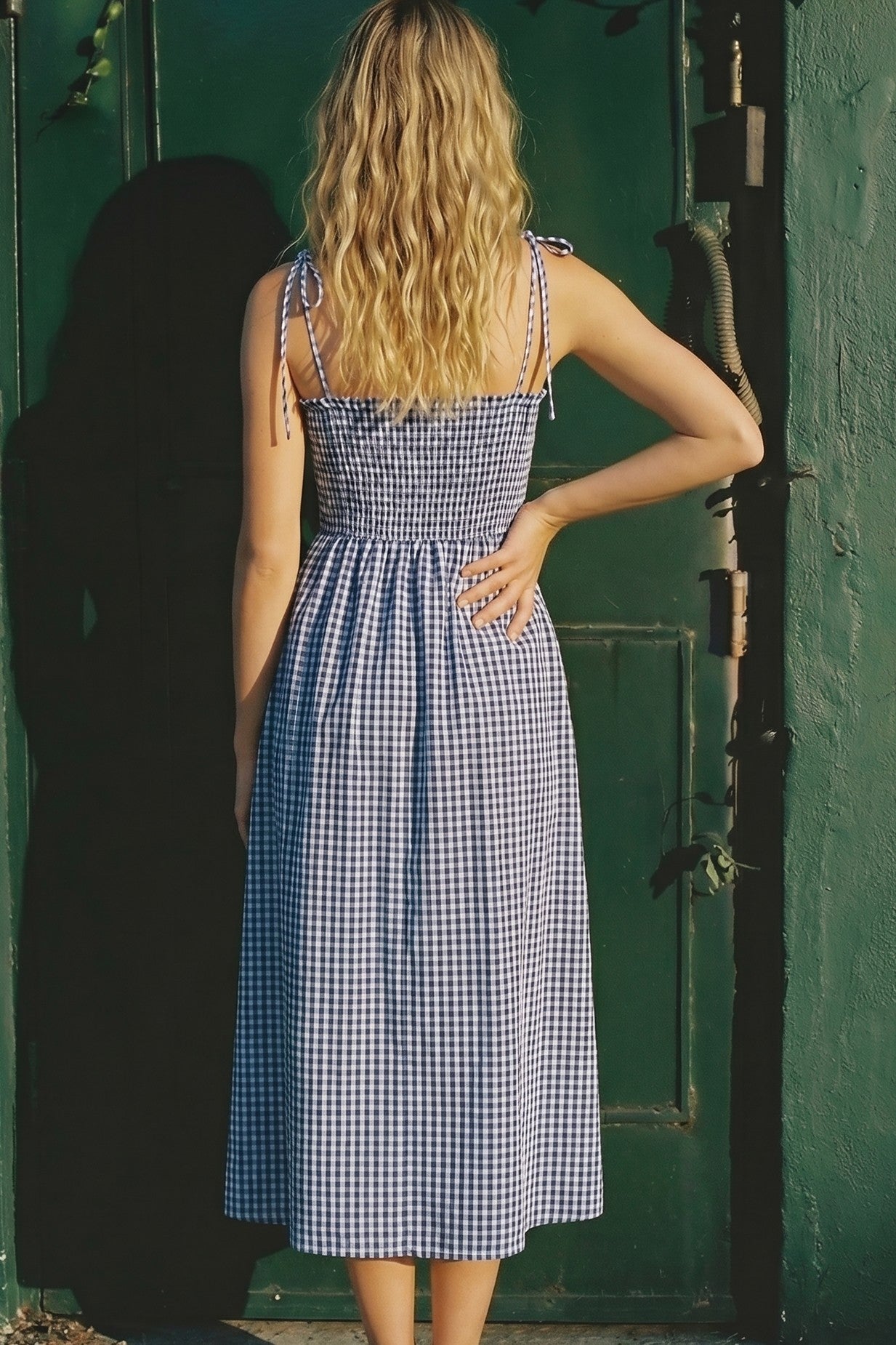 woman wearing a blue and white gingham midi dress with adjustable straps and a smocked back detailing