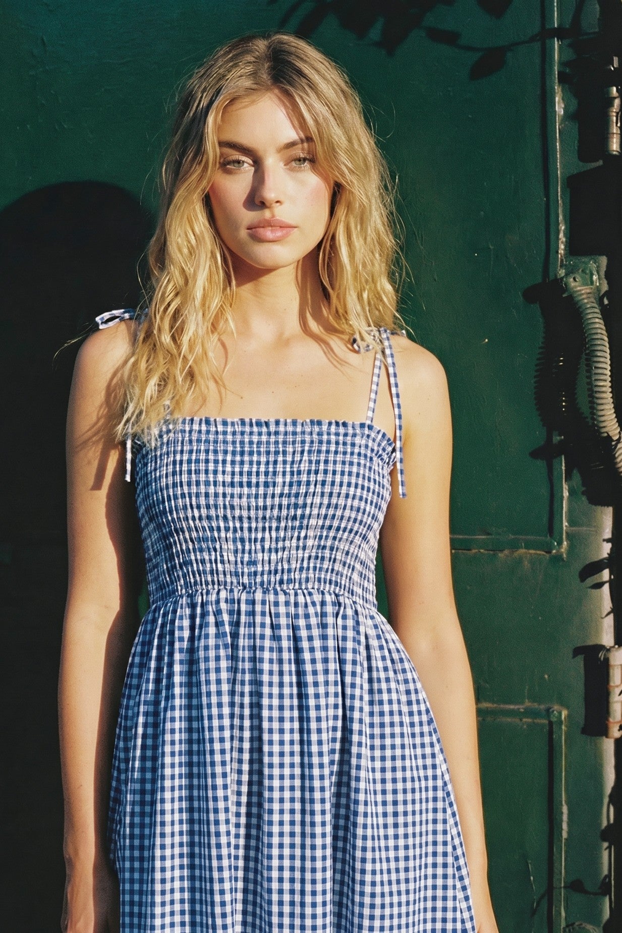 woman wearing a blue and white gingham sundress with smocked bodice and tie straps