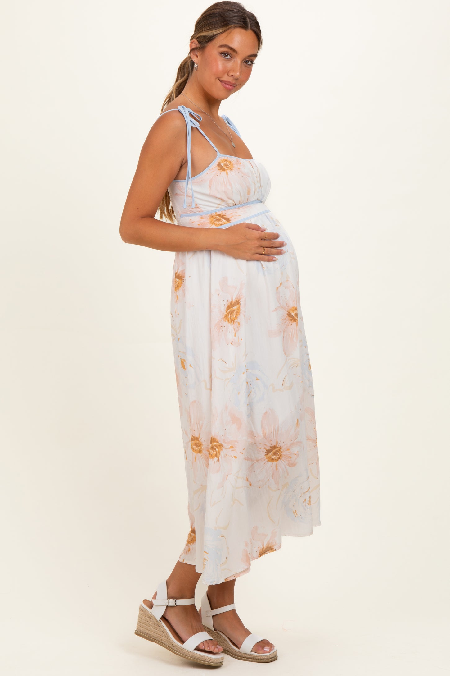 woman wearing a floral print white maternity maxi dress and holding her baby bump