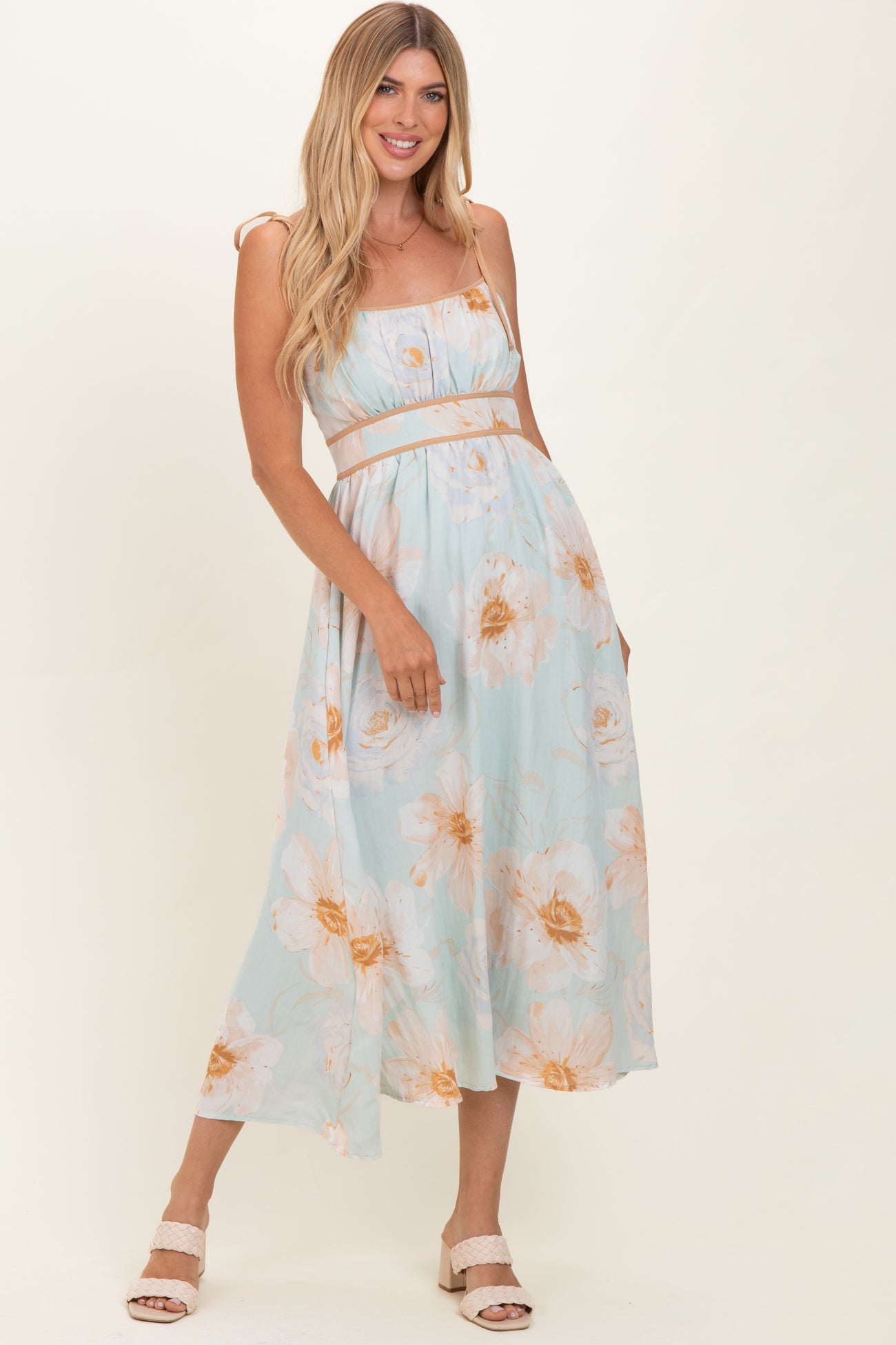 woman wearing a light blue floral midi dress with spaghetti straps and a fitted waist, posing confidently