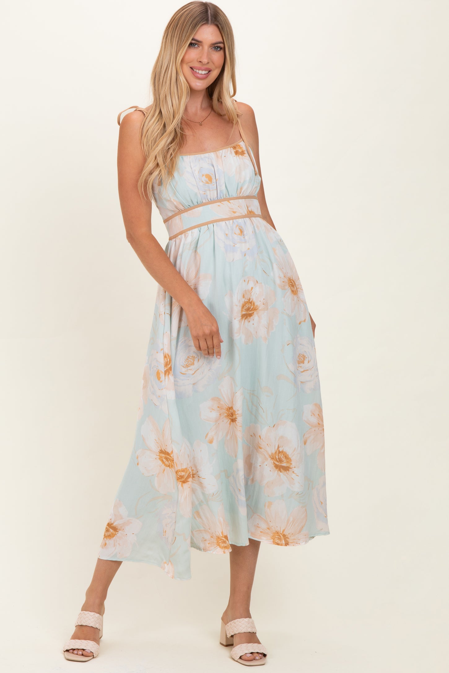woman wearing a light blue floral midi dress with spaghetti straps and a fitted waist, posing confidently