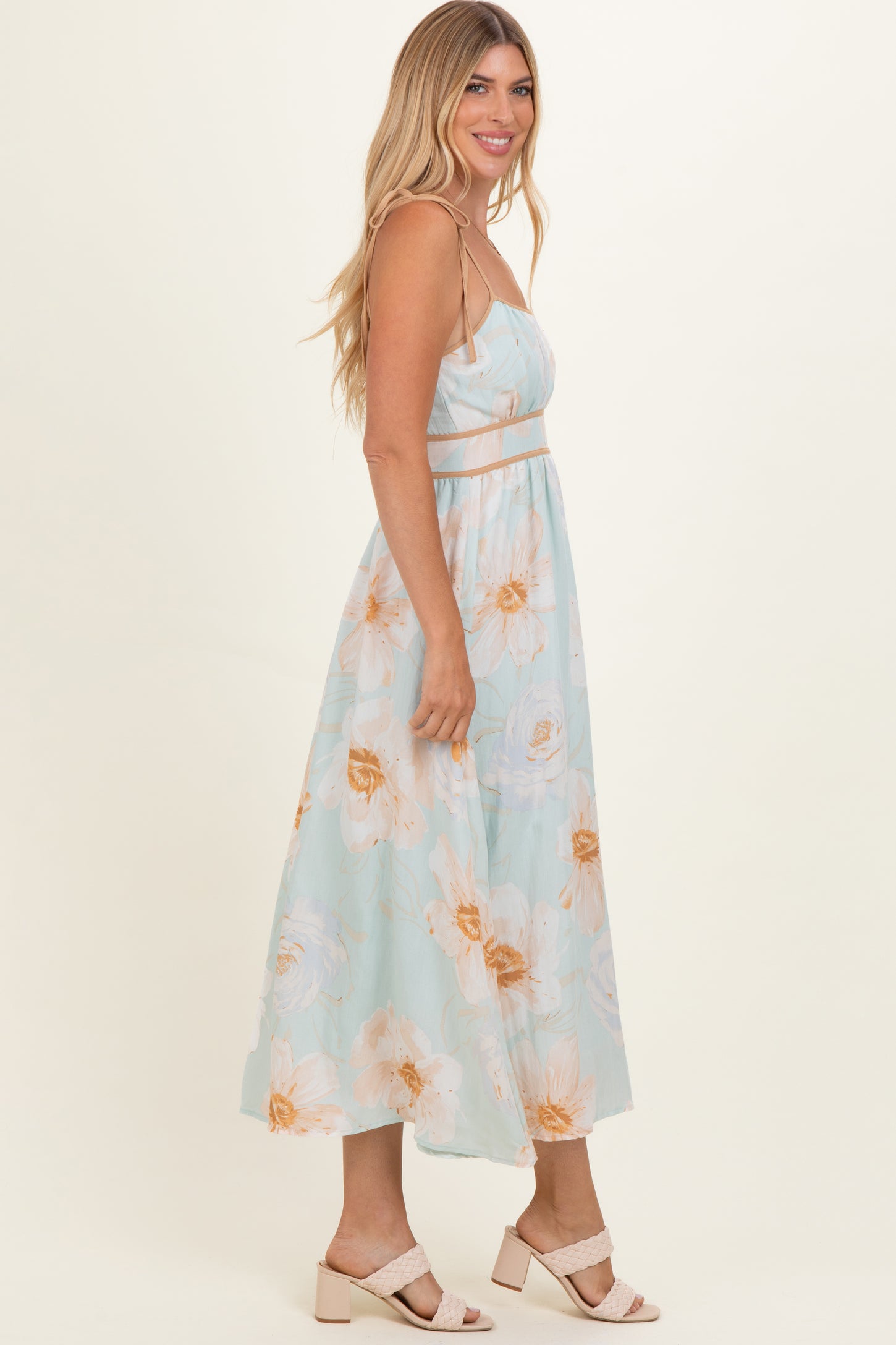 woman wearing a light blue floral maxi dress with spaghetti straps and a fitted waist, standing sideways