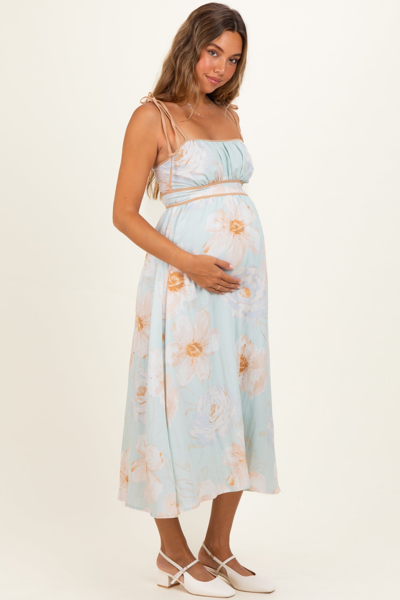 woman wearing a light blue floral maternity dress and holding her baby bump