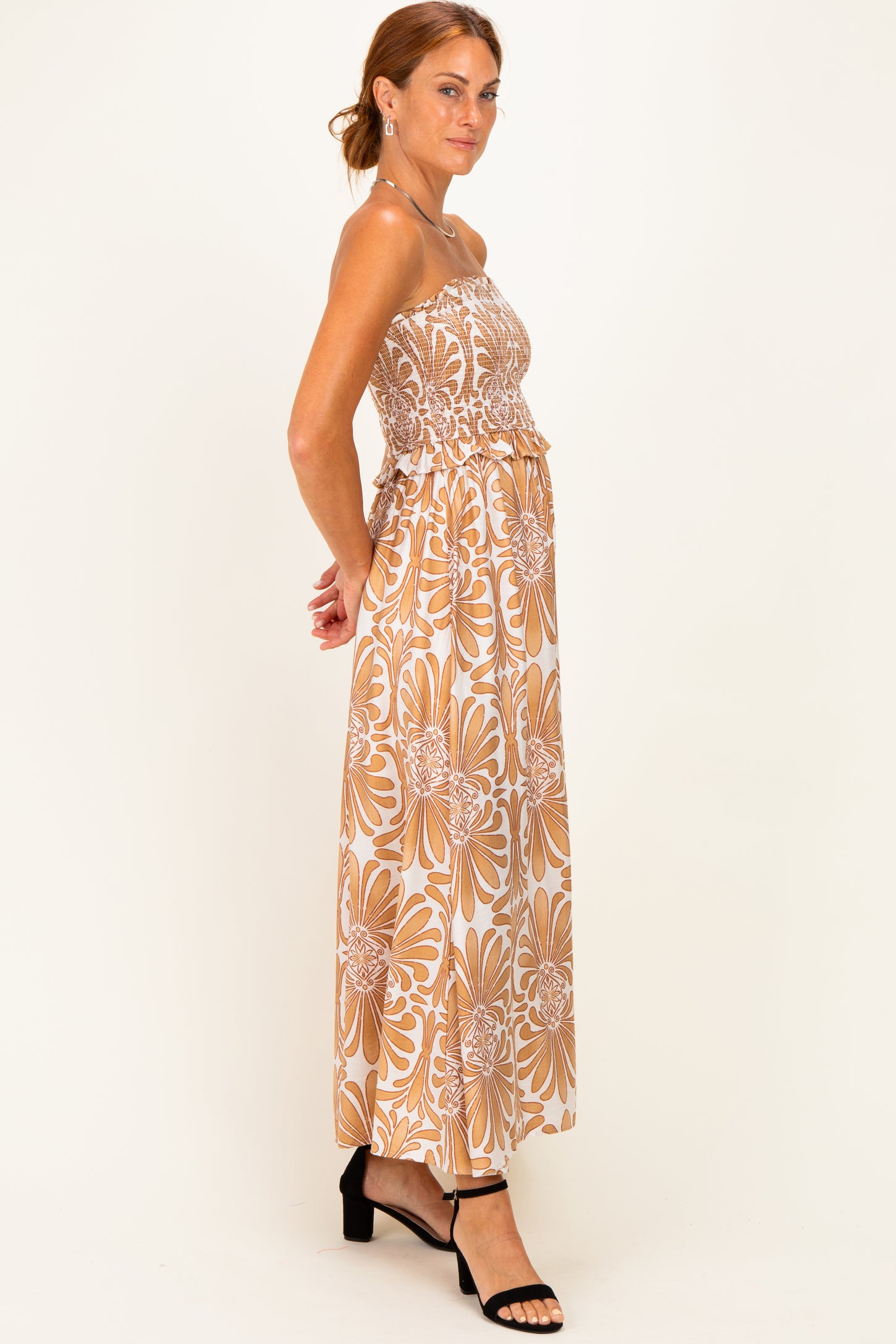 woman wearing a strapless floral maxi dress in brown and white with a ruffled waistline and a flowy silhouette