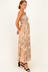 woman wearing a strapless floral maxi dress in brown and white with a ruffled waistline and a flowy silhouette