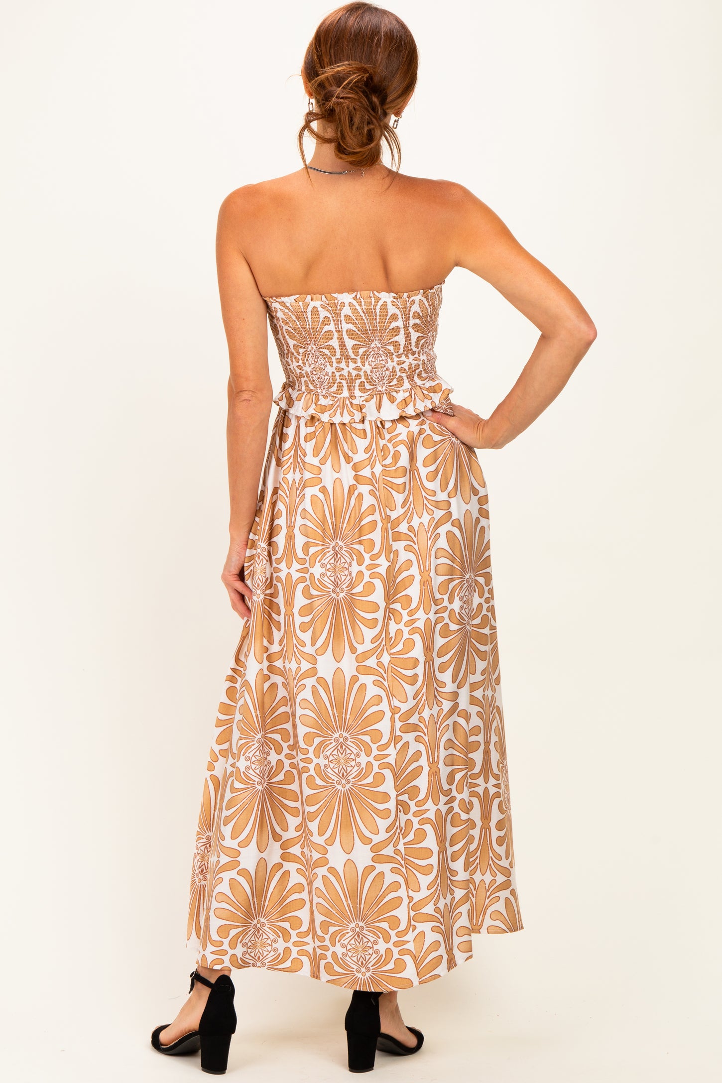woman wearing a strapless maxi dress with a floral print in shades of beige and orange, showing the back view