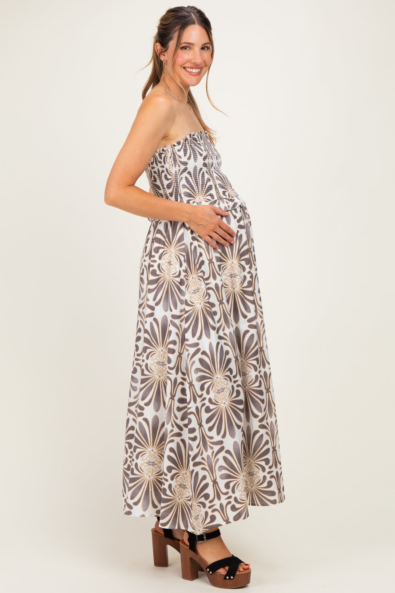 woman wearing a strapless floral print maternity maxi dress and holding her baby bump