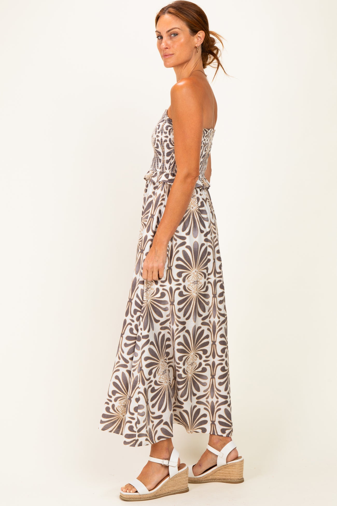woman wearing a strapless brown and white floral maxi dress with a tied waist and strappy white sandals