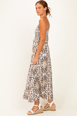 woman wearing a strapless brown and white floral maxi dress with a tied waist and strappy white sandals