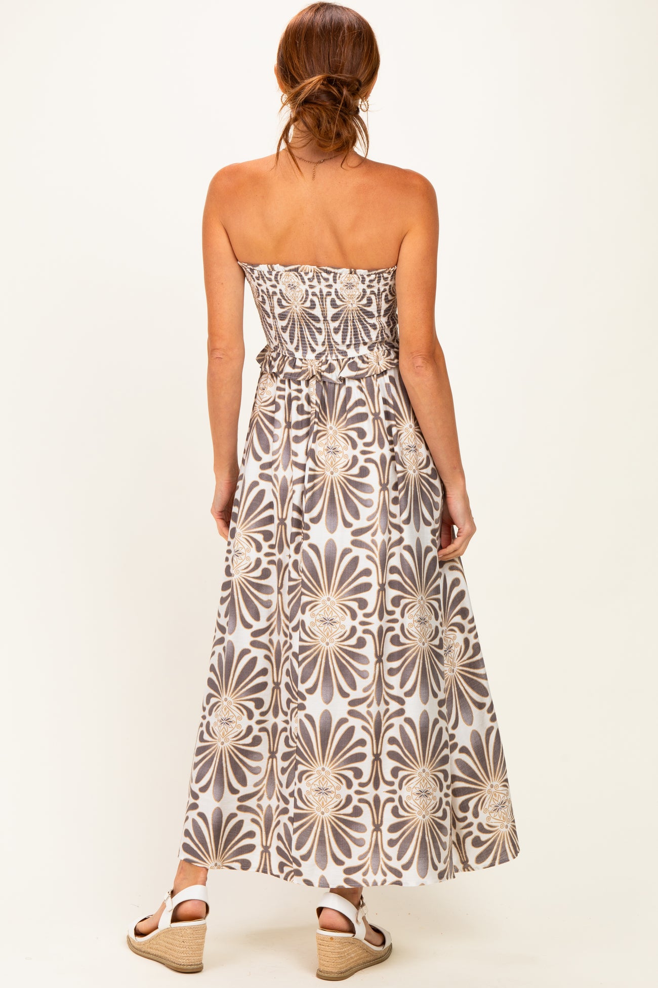 woman wearing a strapless maxi dress with a floral pattern in shades of gray and beige