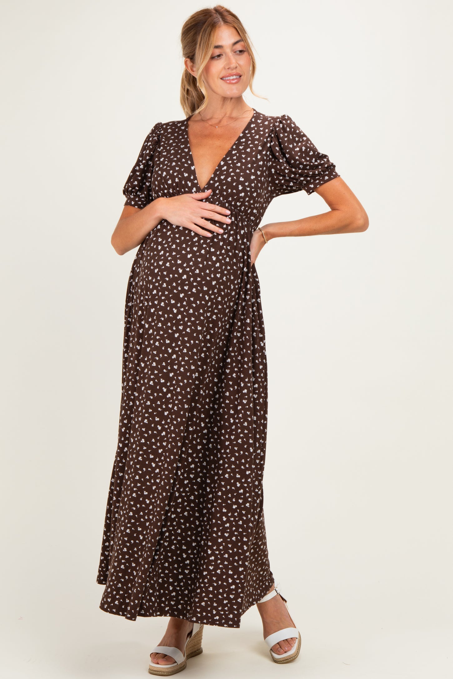woman wearing a brown polka dot maternity maxi dress and posing with her baby bump visible