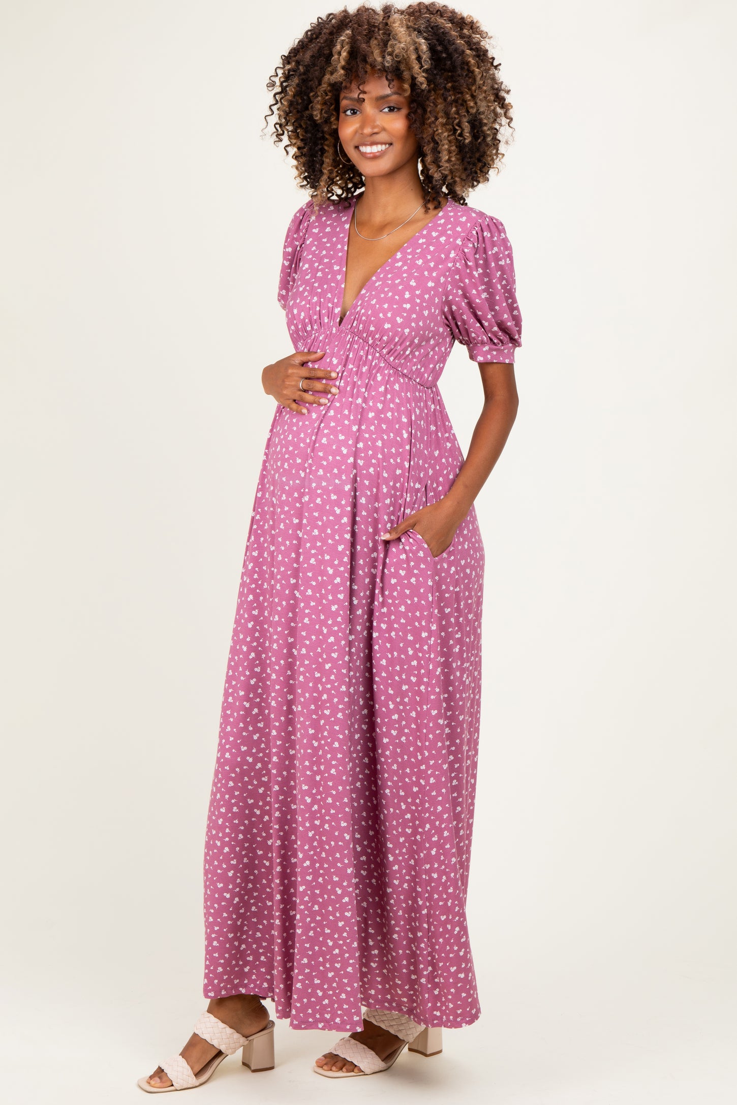 woman wearing a pink polka dot maternity maxi dress, with puff sleeves and pockets, showing her baby bump