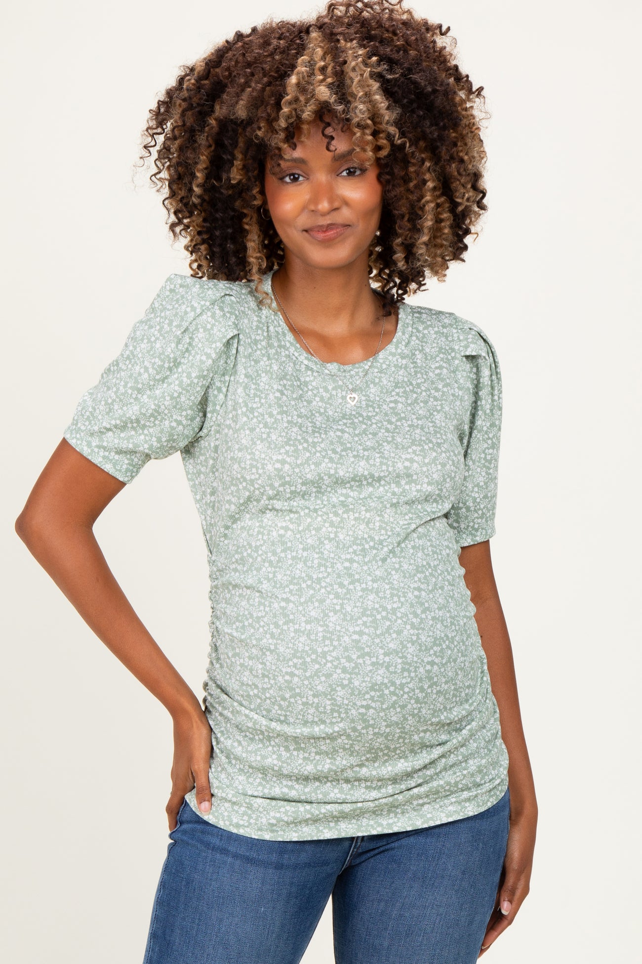 woman wearing a green floral maternity top with puff sleeves and a visible baby bump, paired with blue jeans