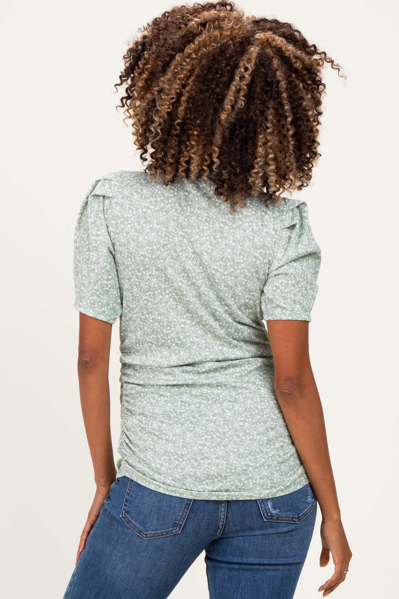 woman wearing a light green floral maternity top with puff sleeves and ruched sides, showing her baby bump from the back