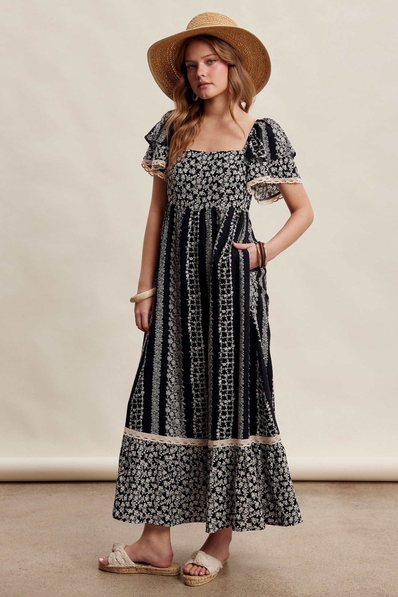 woman wearing a black and white floral maxi dress with ruffle sleeves and a wide-brim straw hat