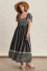 woman wearing a navy blue floral maxi dress with puff sleeves and a tiered skirt, styled with a straw hat and sandals