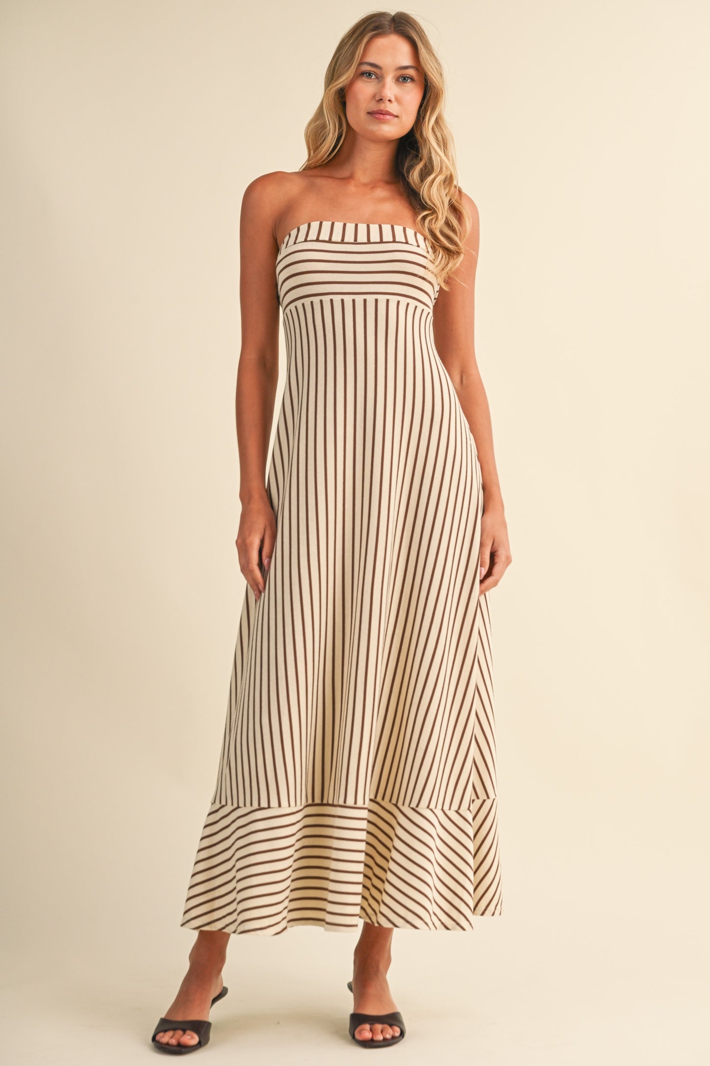woman wearing a cream and brown striped strapless maxi dress with a flared hemline and a relaxed fit