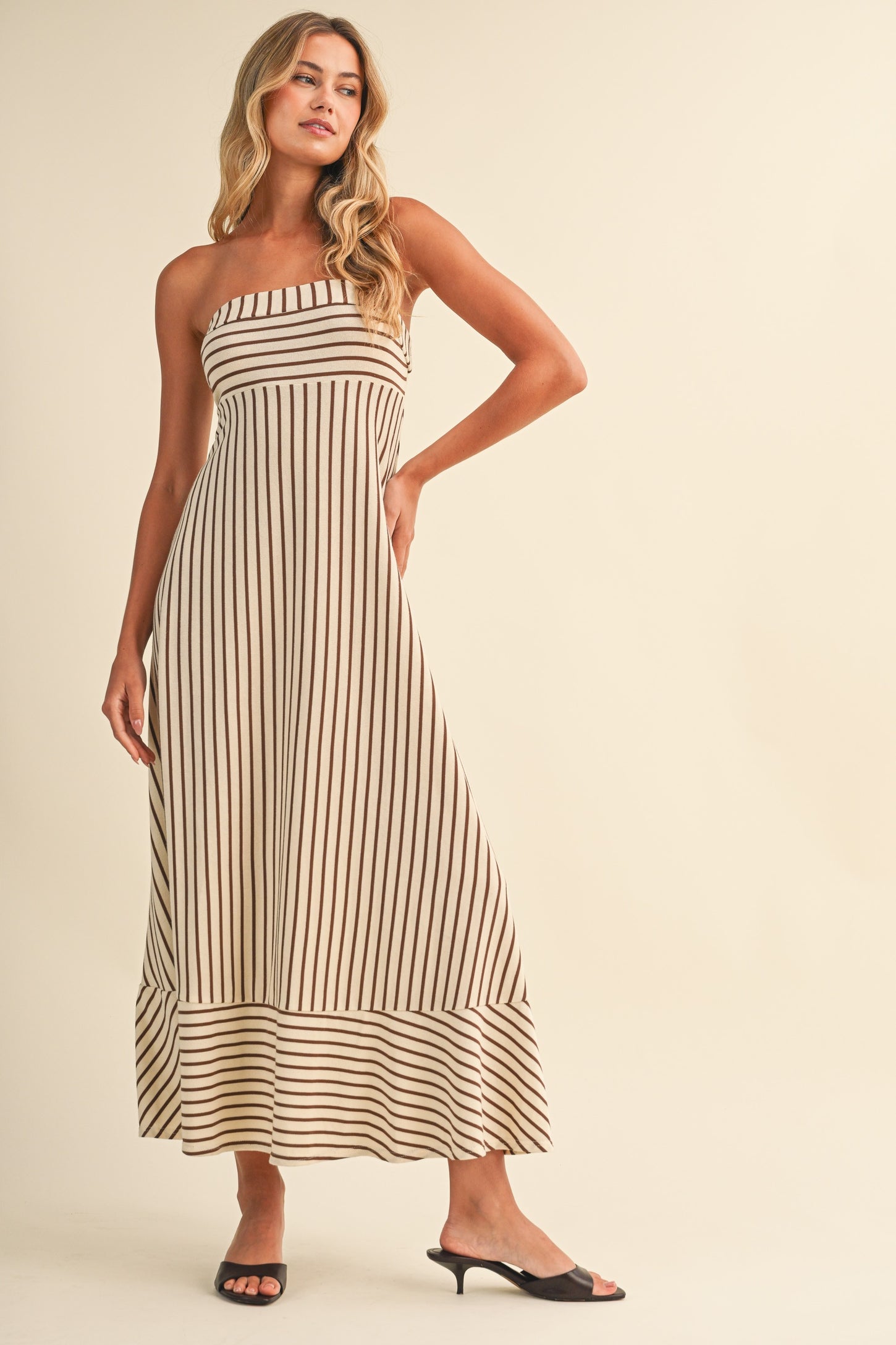 woman wearing a striped strapless maxi dress with a flared hem and black slide sandals