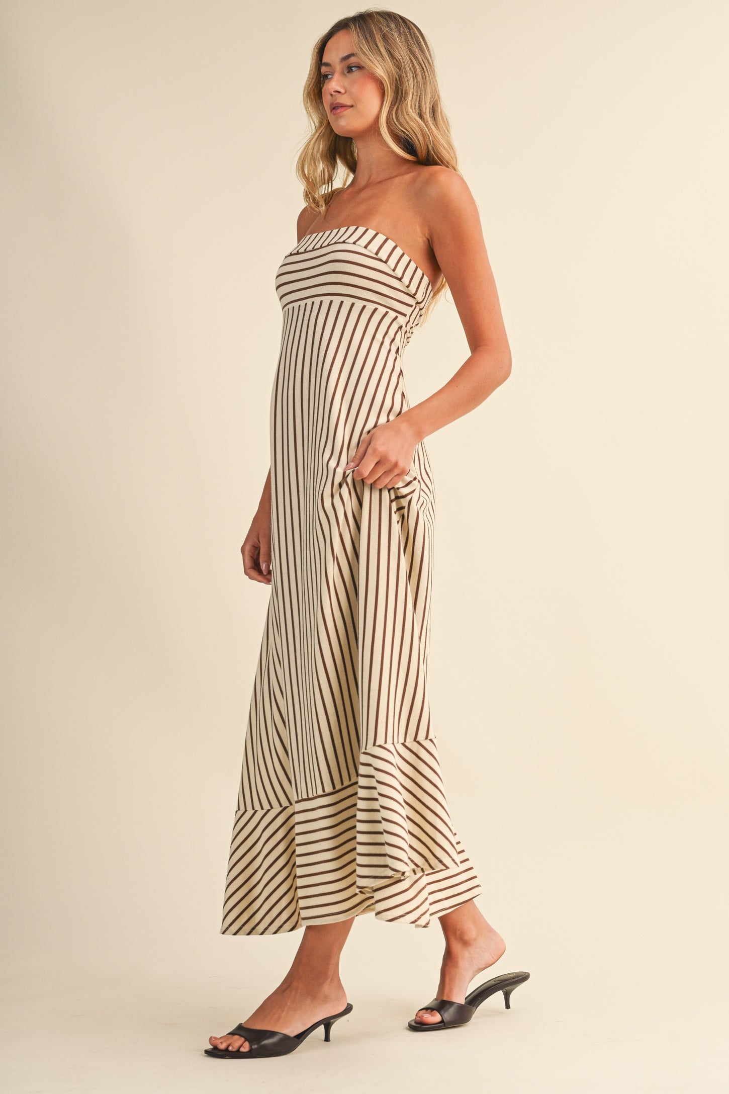woman wearing a beige and brown striped strapless maxi dress with a flared hem and side pockets