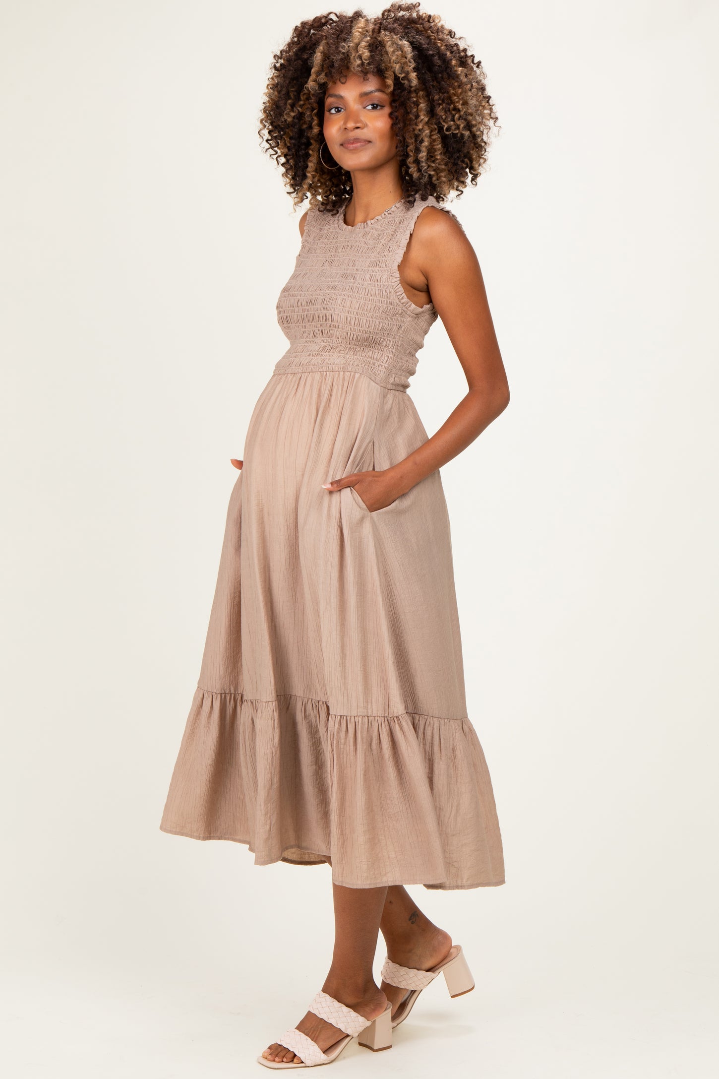 woman wearing a light brown maternity dress with a smocked bodice, tiered skirt, and pockets, showing her baby bump