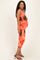 woman wearing a tie-dye orange maternity dress with a visible baby bump and brown strappy heels