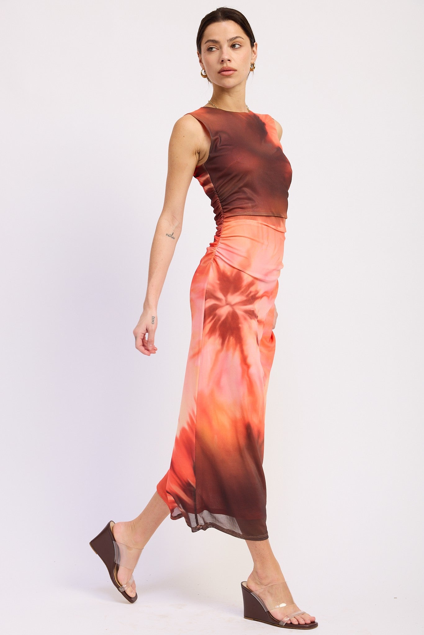 woman wearing a brown and orange tie-dye midi dress with a fitted bodice and side ruching, walking gracefully