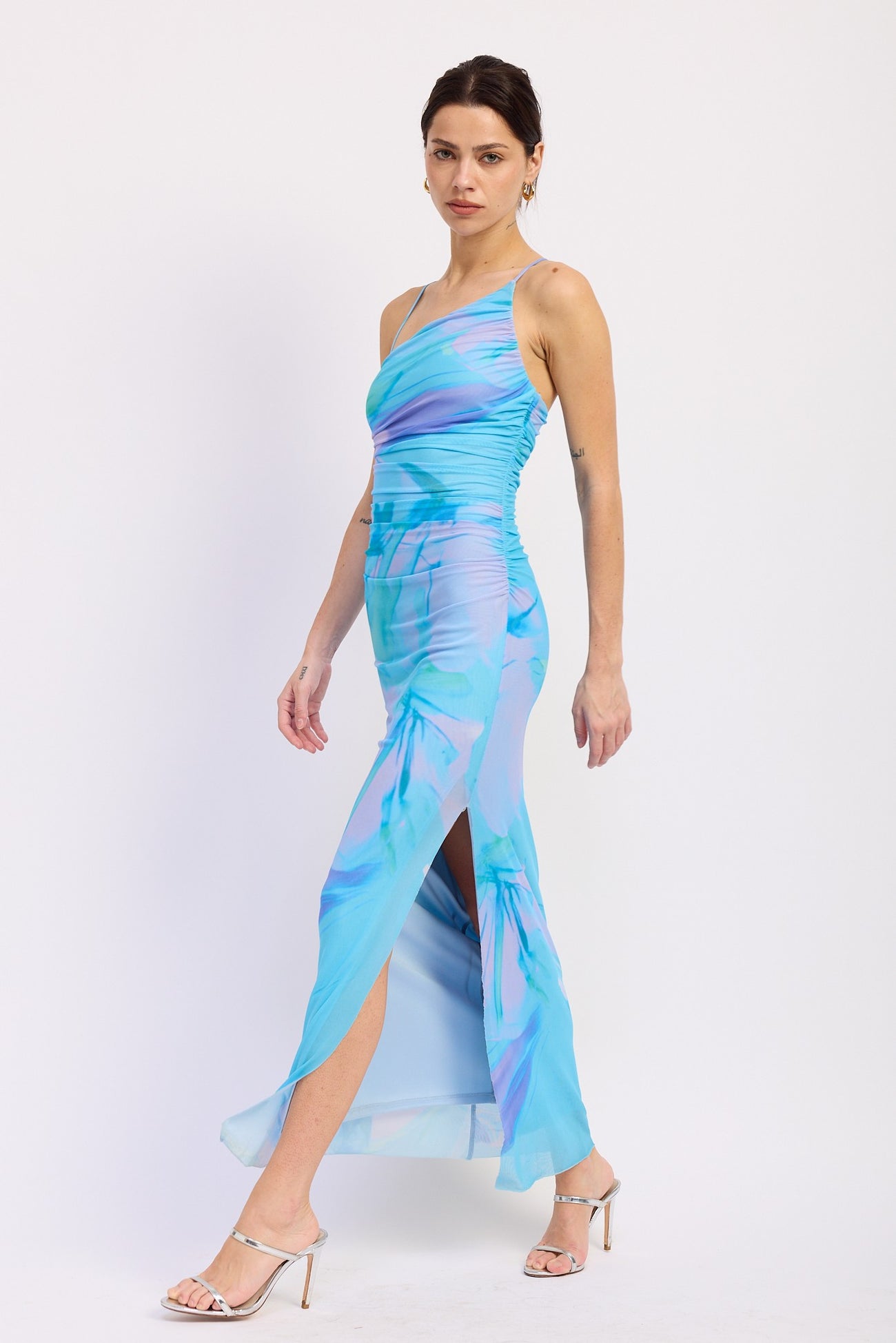 woman wearing a blue and purple floral print maxi dress with ruching and high slits, paired with silver heels