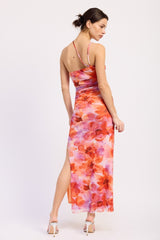 woman wearing a floral maxi dress with orange and pink hues and a thigh-high slit, styled with strappy heels