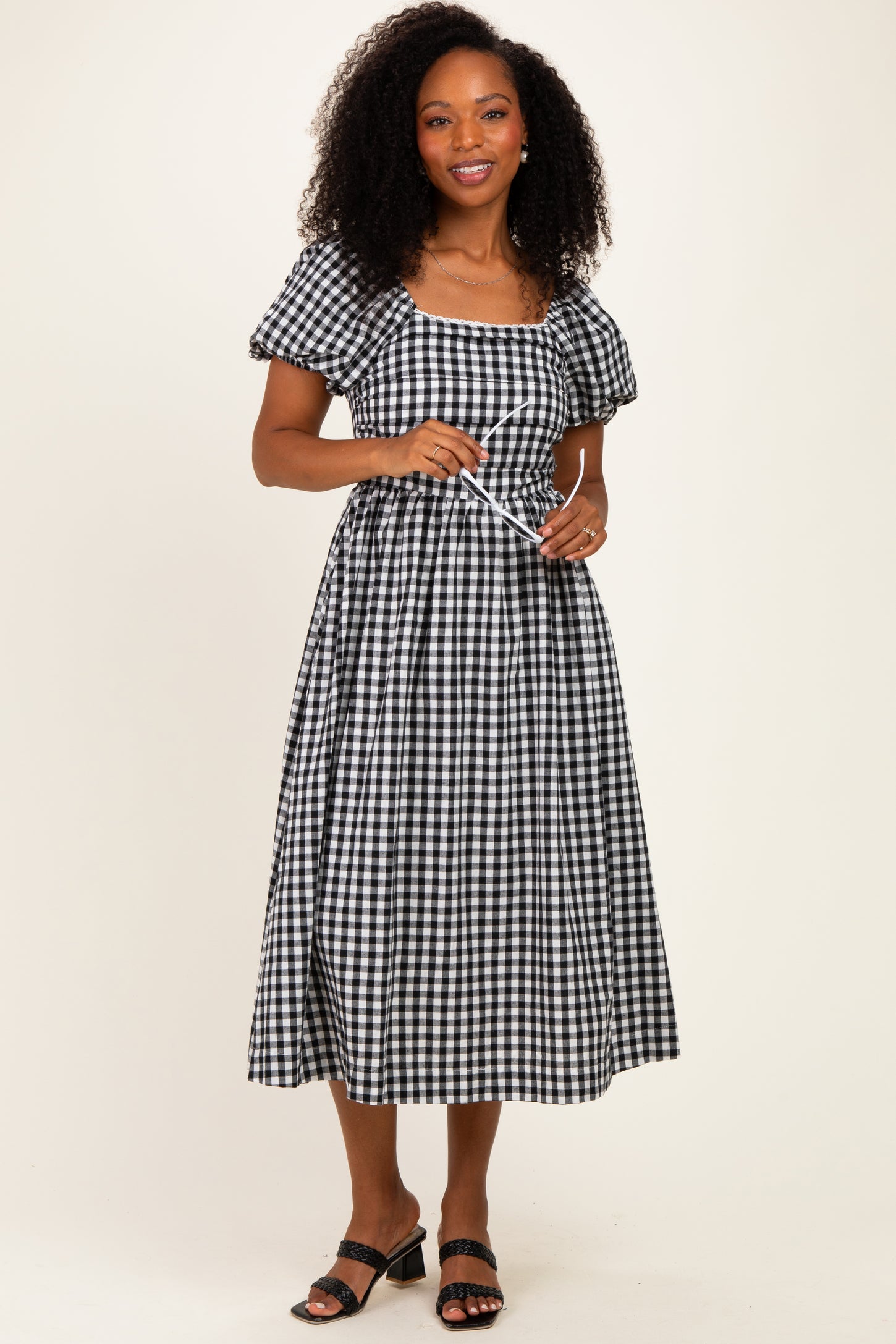 woman wearing a black and white gingham midi dress with puff sleeves and a tie waist detail