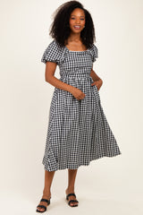 woman wearing a black and white gingham midi dress with puff sleeves and a fitted waist, posing with one hand on her hip