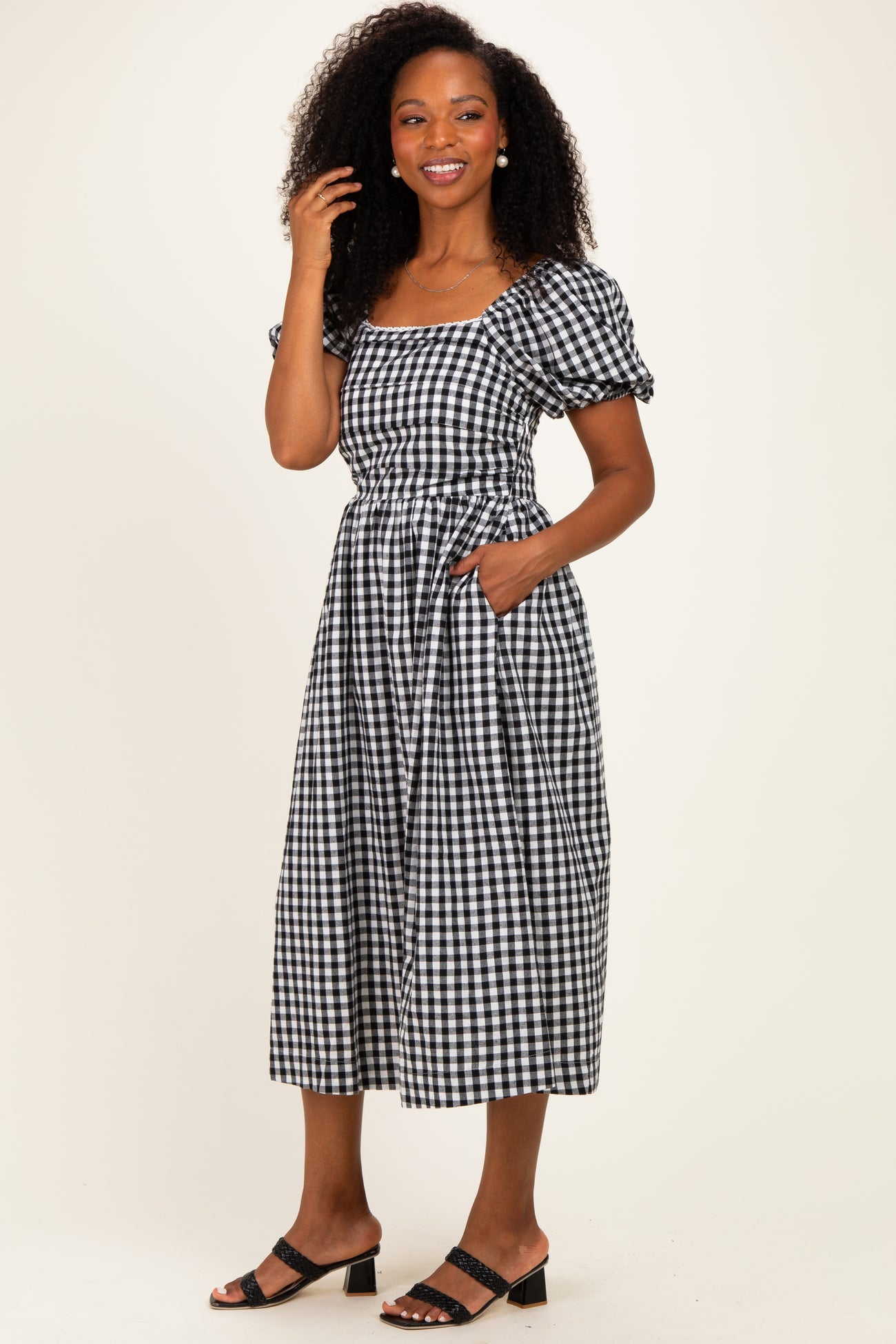 woman wearing a black and white gingham midi dress with puff sleeves and pockets, standing and smiling