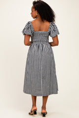 woman wearing a black and white gingham midi dress with puff sleeves and a smocked back, standing with her back to the camera