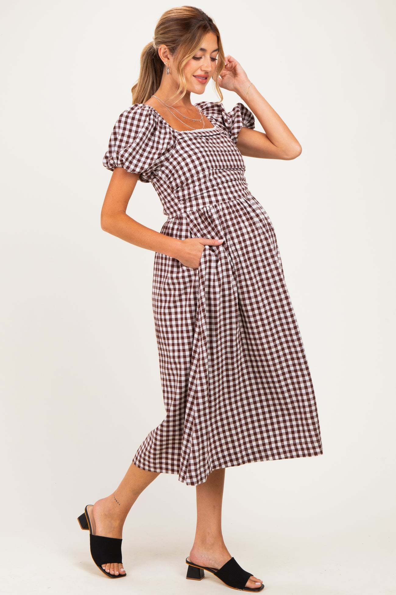woman wearing a brown and white checked maternity dress with puff sleeves and pockets, showing her baby bump
