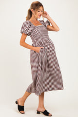 woman wearing a brown and white checked maternity dress with puff sleeves and pockets, showing her baby bump