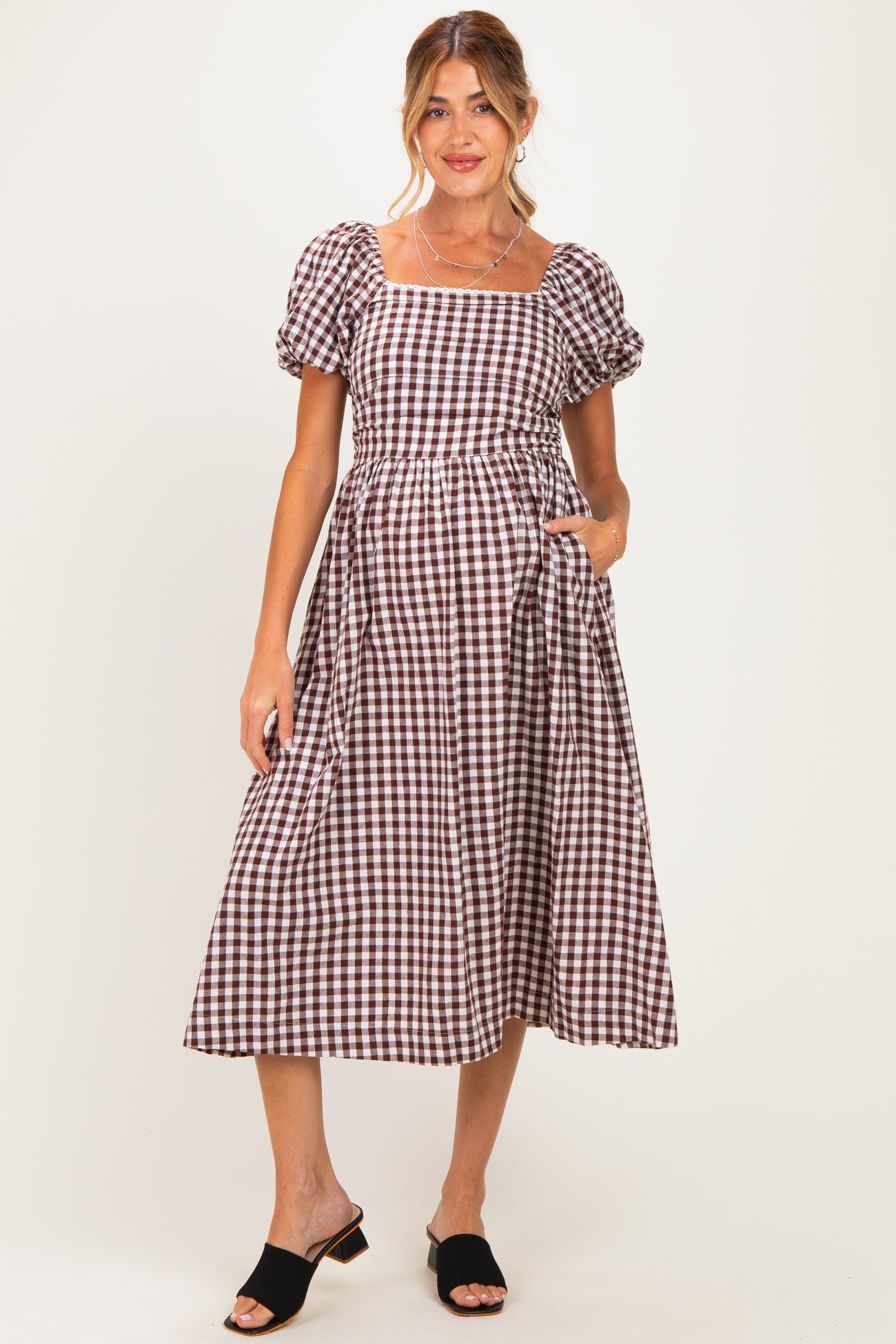 woman wearing a brown and white checkered maternity dress with puff sleeves and pockets, showing her baby bump