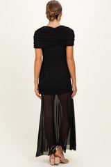 woman wearing a black maternity dress with ruched short sleeves and a sheer maxi skirt, showing a baby bump from the back