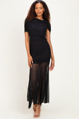 woman wearing a black ruched maxi dress with sheer overlay and short sleeves, standing against a neutral background