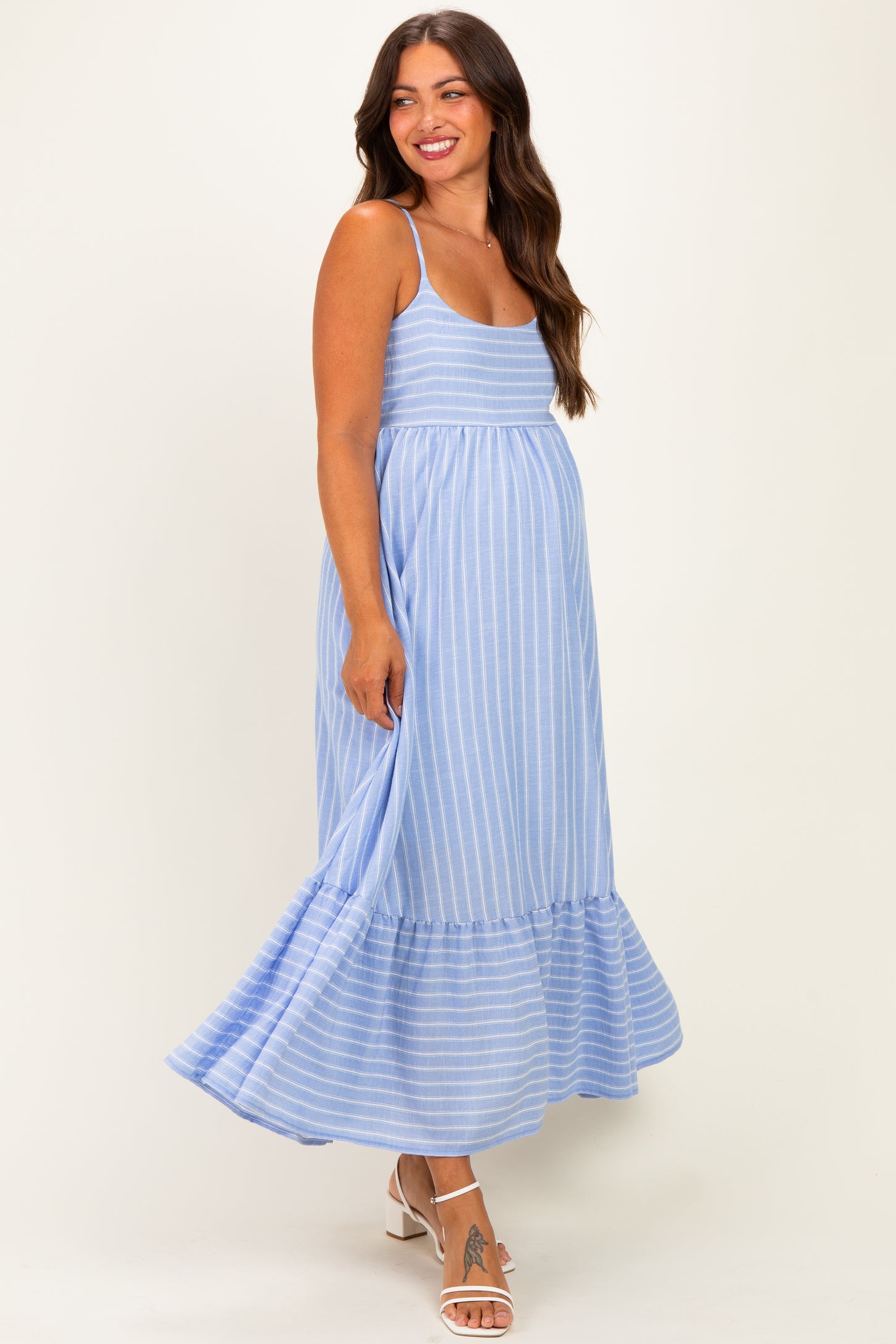 woman wearing a light blue striped maternity maxi dress with a ruffled hem and a visible baby bump