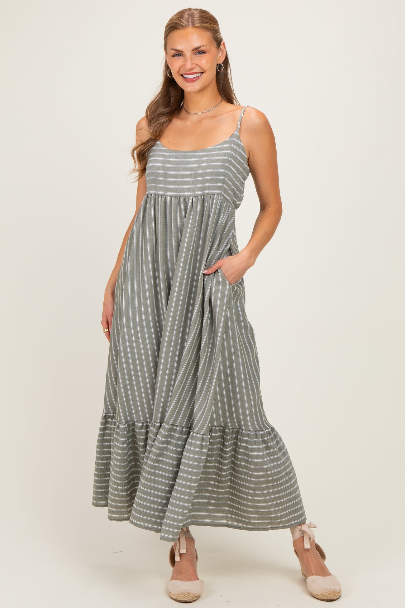 woman wearing a grey striped maxi dress with a ruffled hem and pockets, smiling at the camera