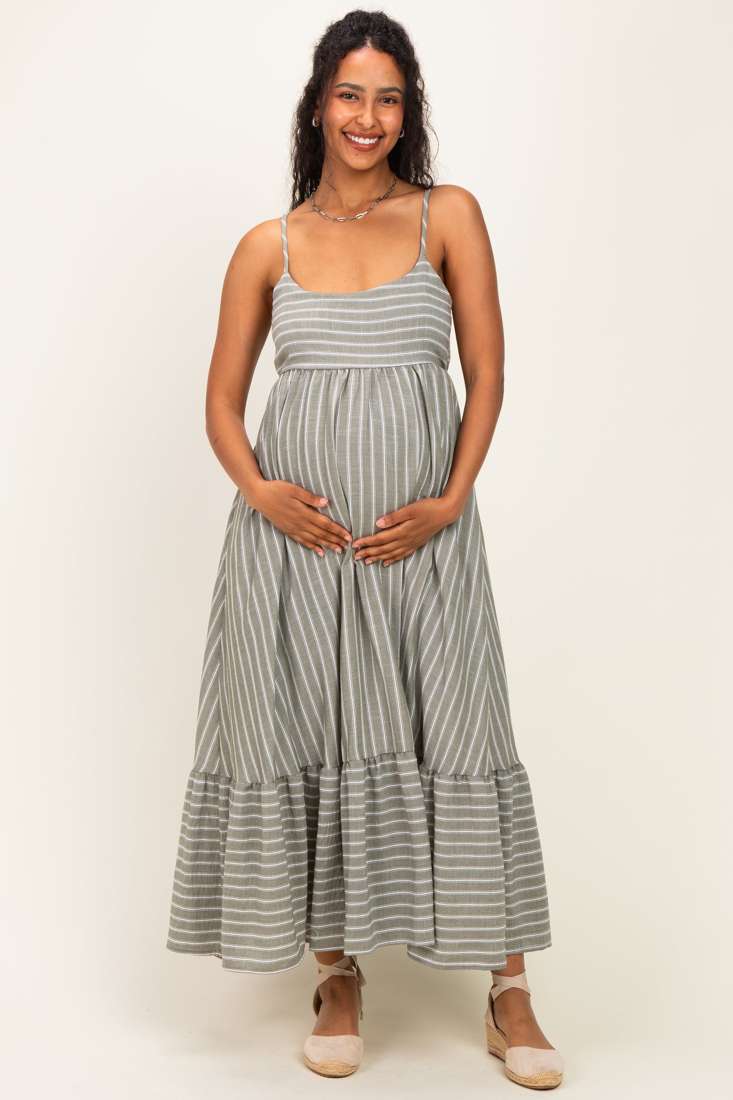 woman wearing a gray and white striped maternity dress with a tiered hem and holding her baby bump