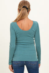 woman wearing a teal long sleeve maternity top with a scoop back and ribbed texture, styled with jeans