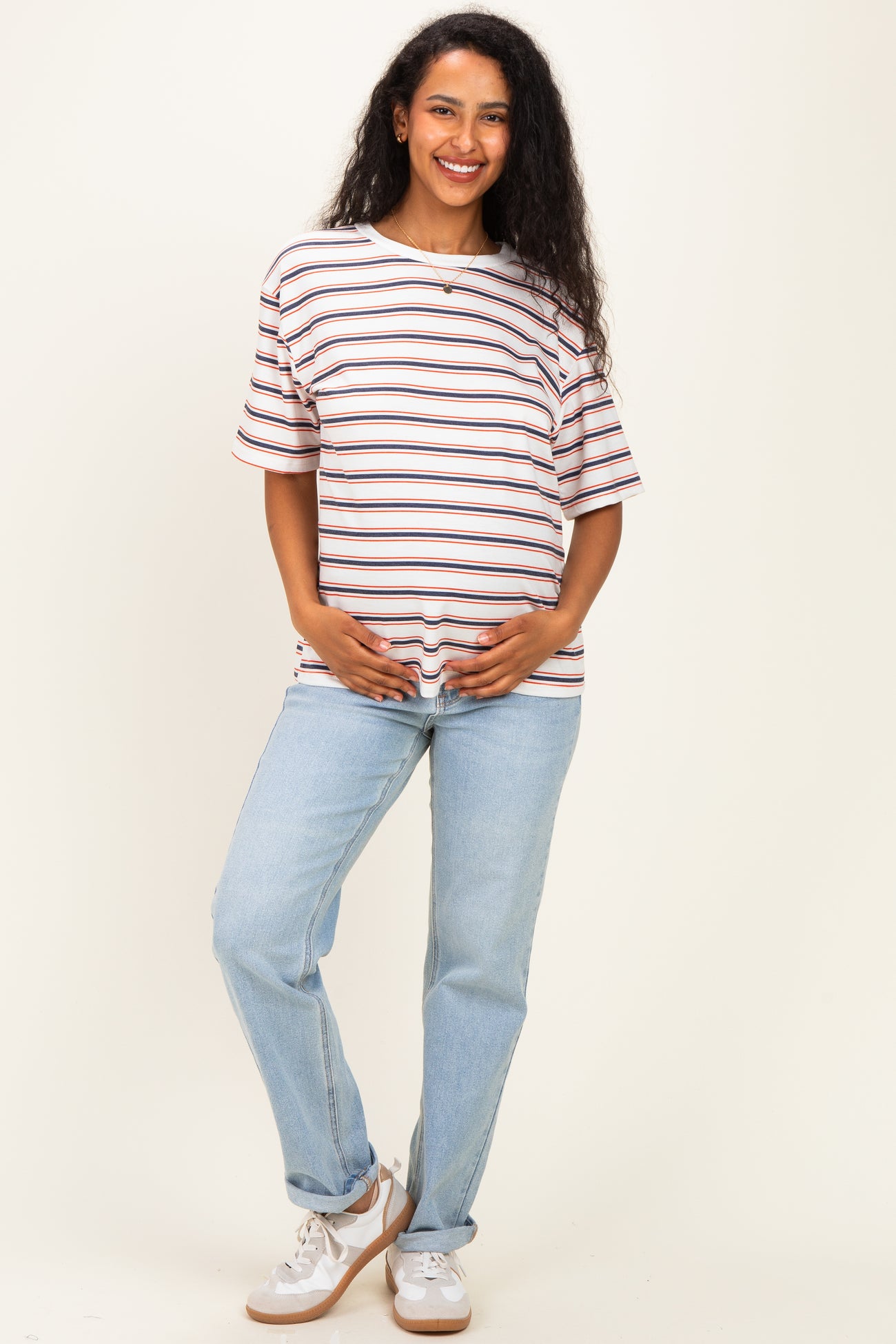 woman wearing a striped maternity t-shirt and light blue jeans, gently holding her baby bump