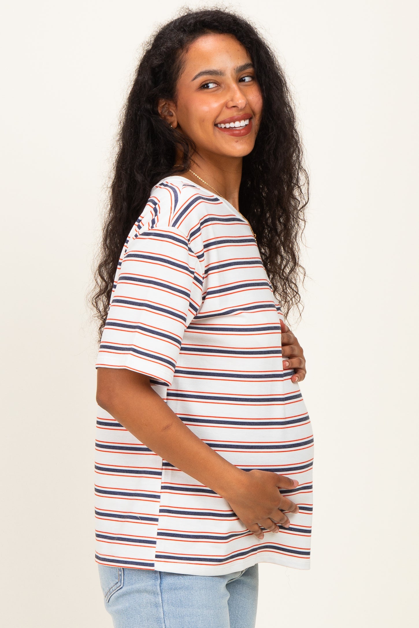 woman wearing a striped maternity top with a loose fit, gently holding her baby bump while smiling