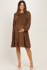 woman wearing a brown floral maternity dress with long sleeves, smiling and holding her baby bump